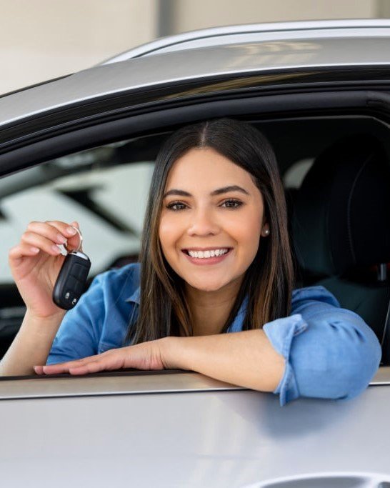 Happy Latin American woman holding the keys of her new car at the dealership - car ownership concepts